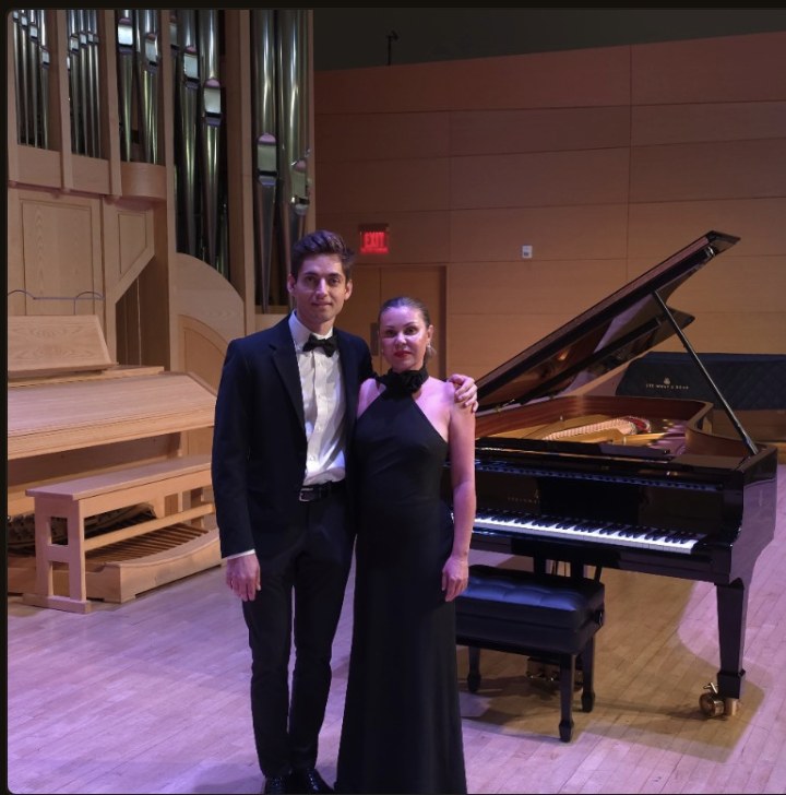 Artem Alexanian and guest in formal attire on stage beside a Steinway grand piano with pipe organ backdrop