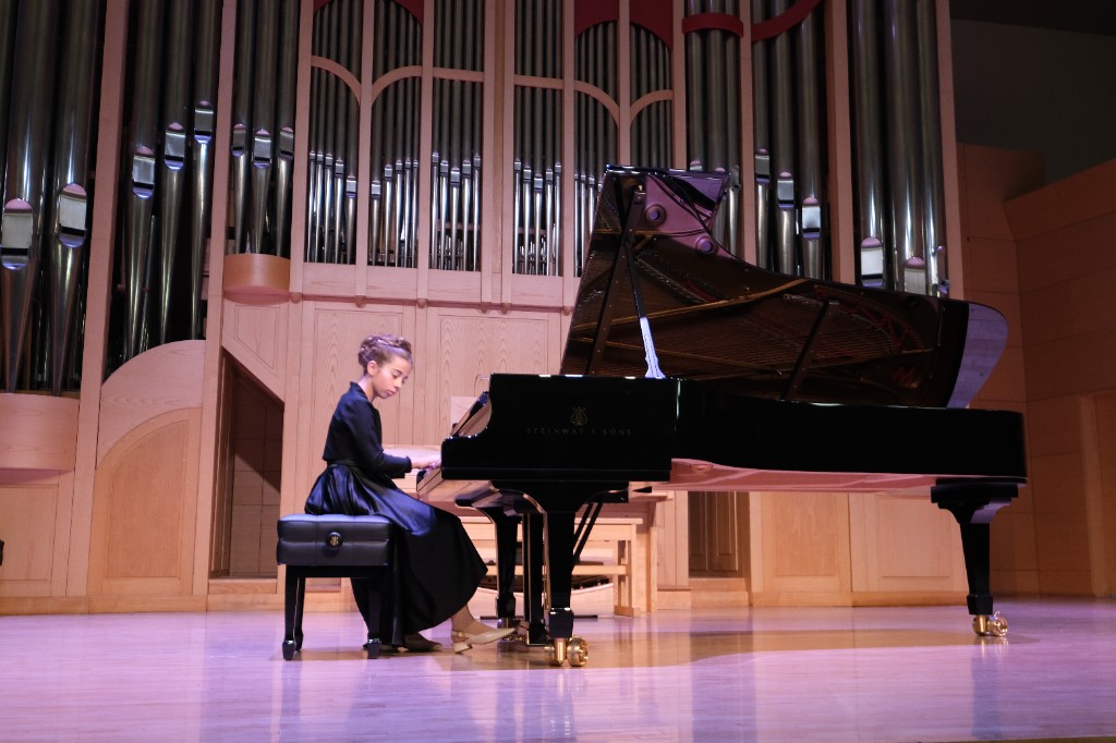 Student in formal attire performing at a grand piano