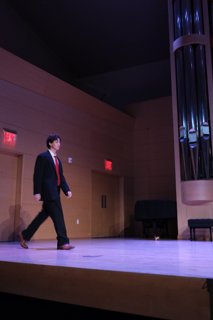 Student in formal attire walking across the recital stage